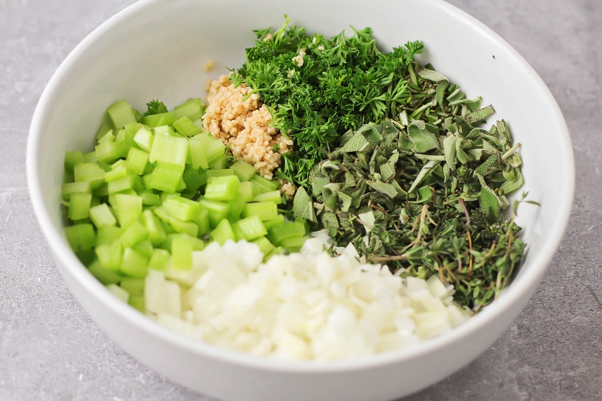 Fresh herbs and veggies chopped in a white bowl for homemade stuffing
