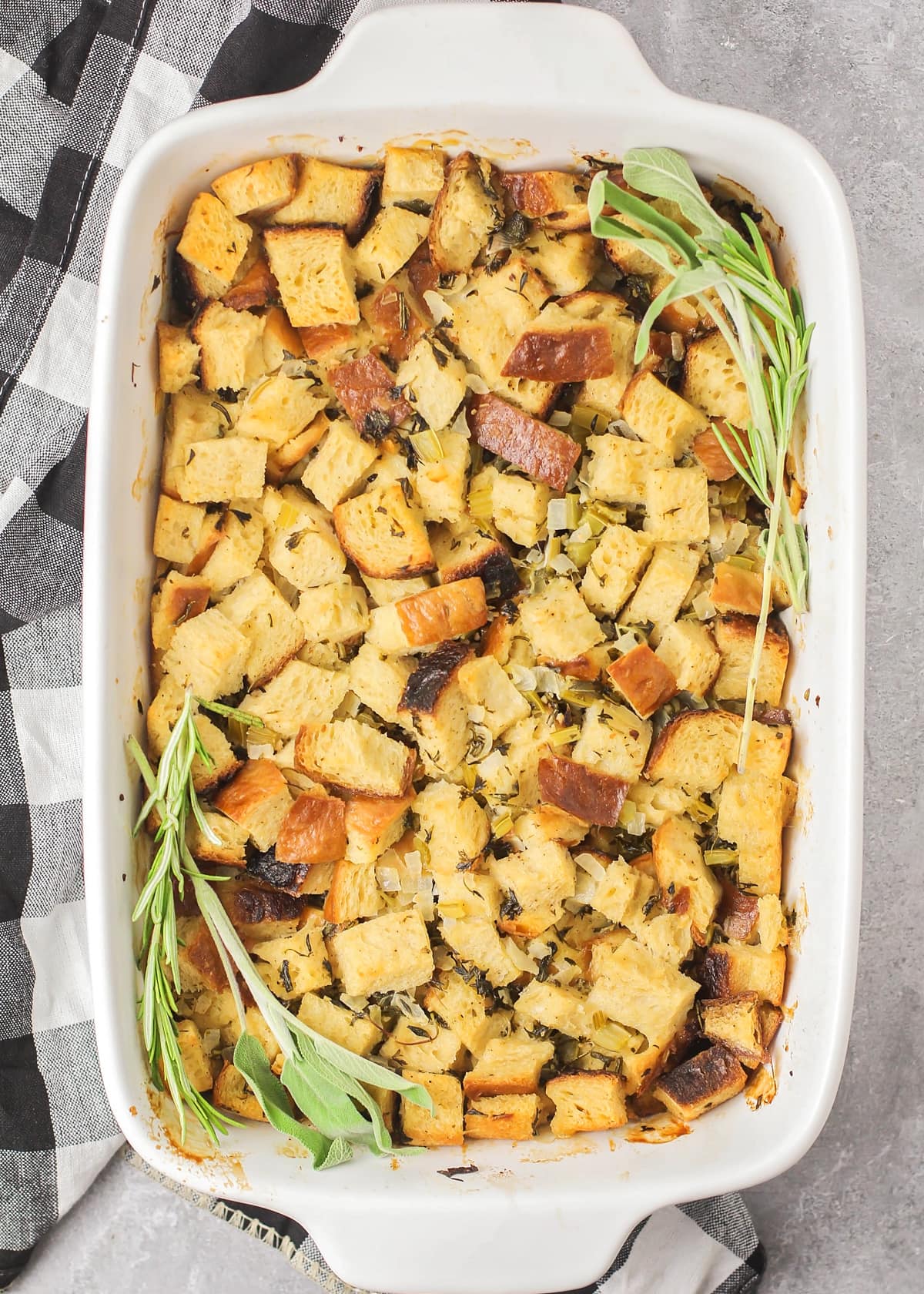 Cooked homemade stuffing in a white baking dish topped with fresh herbs.