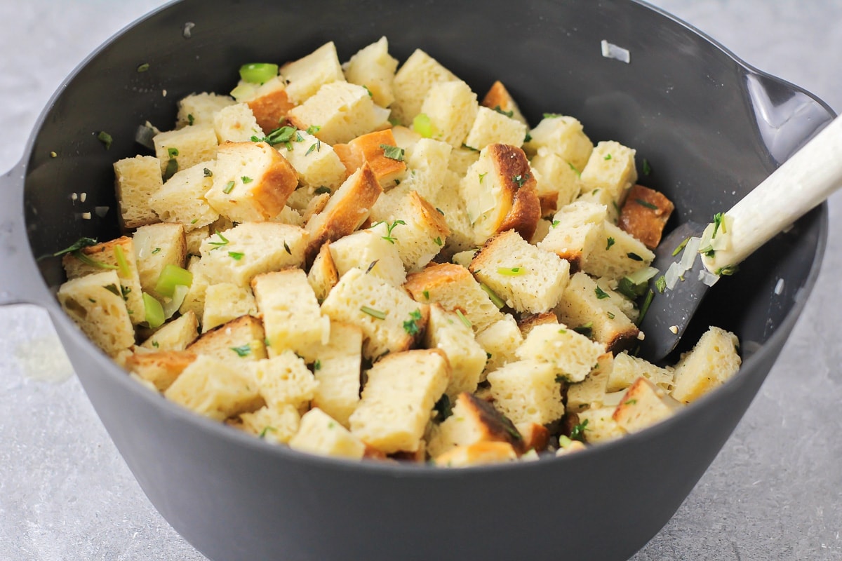 Mixing bread cubes and cooked veggies in a grey bowl.