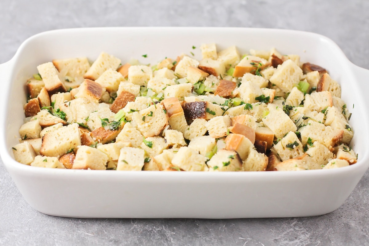 Spreading seasoned bread cubes in a white baking dish for homemade stuffing.