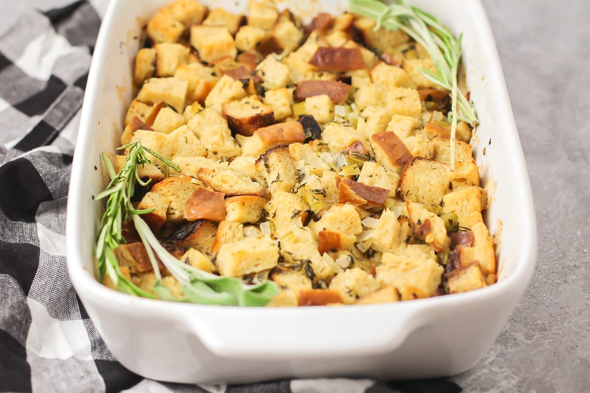 Homemade stuffing in a white baking dish, seasoned with fresh herbs.