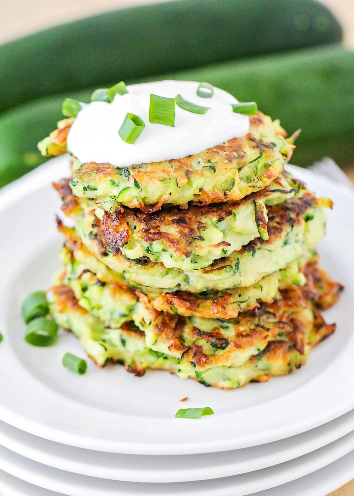 Close up of a stack of zucchini fritters topped with sour cream and green onions.