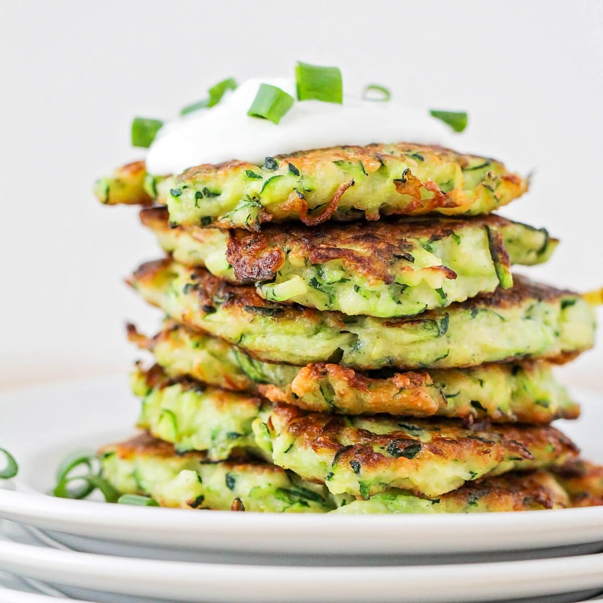 Close up of zucchini fritters stacked and topped with sour cream.