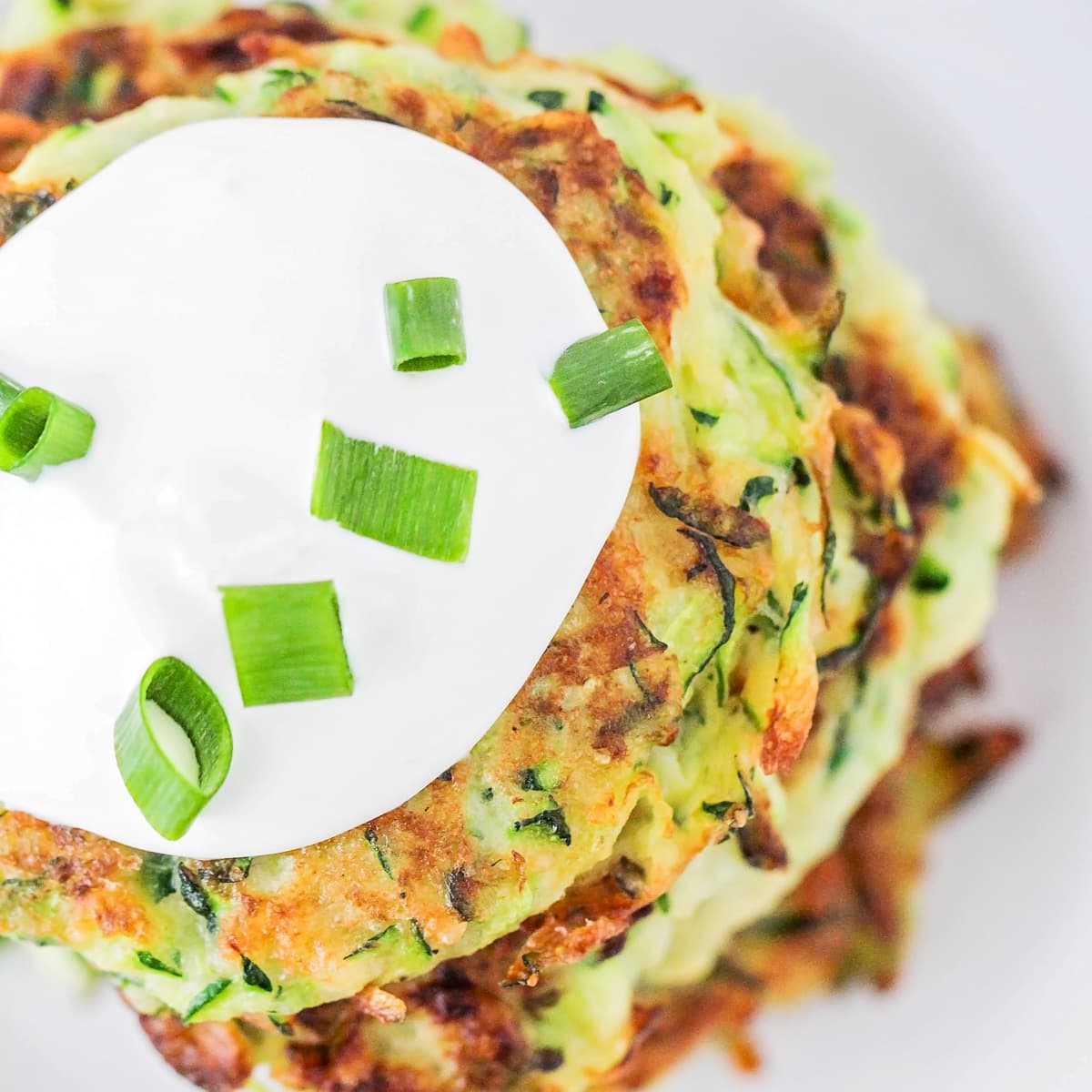 Top view of zucchini pancakes topped with sour cream.
