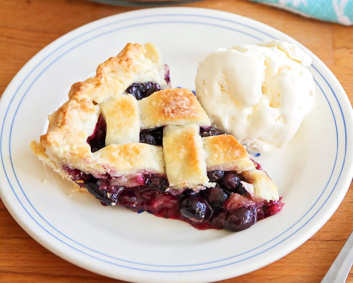 A slice of fresh blueberry pie with a side of vanilla ice cream.