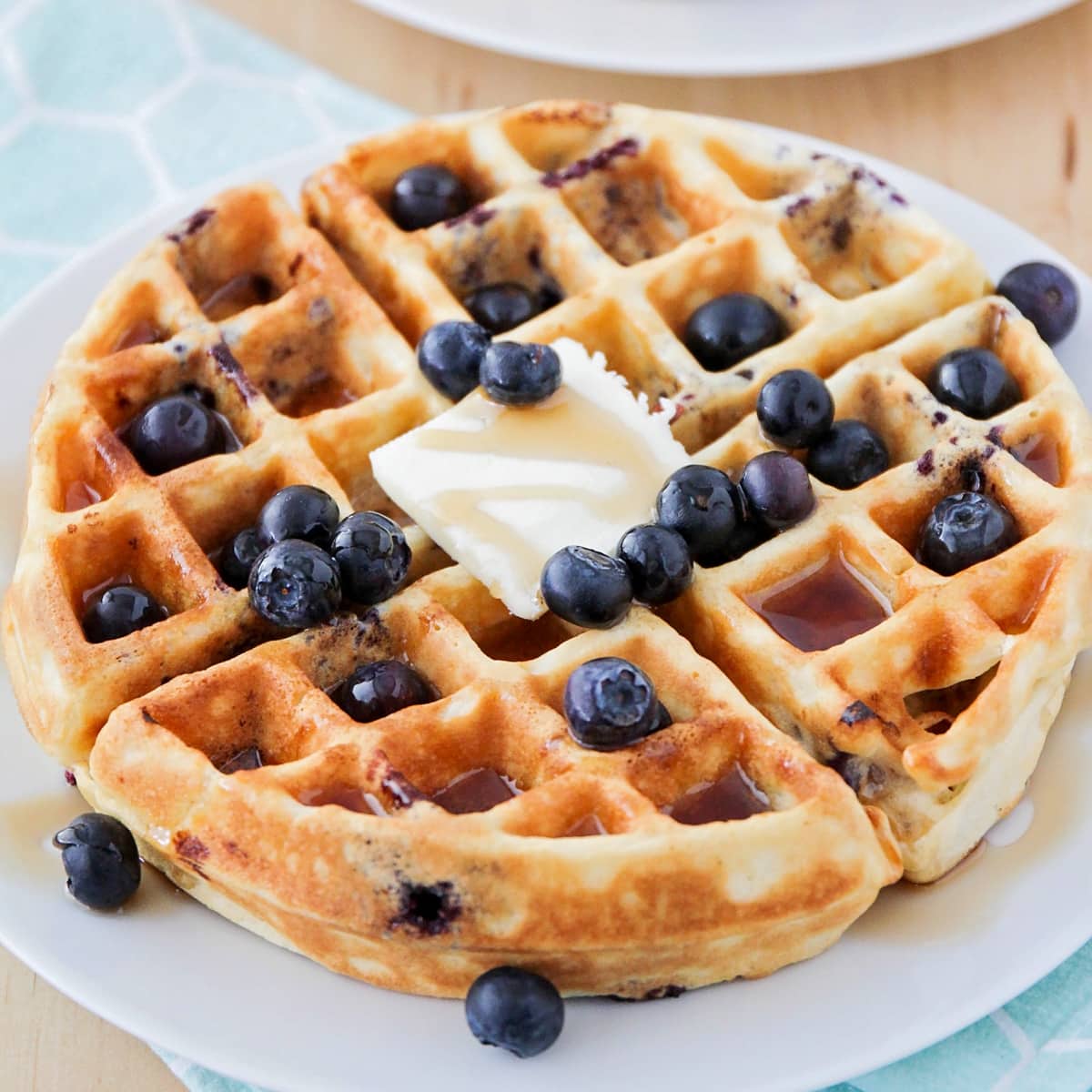 Close up of blueberry waffles topped with butter, syrup, and fresh blueberries.