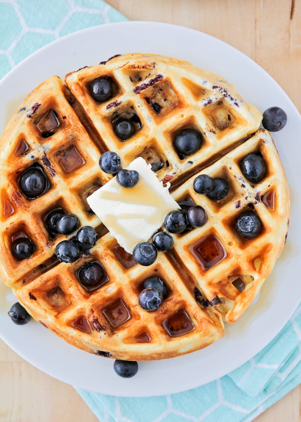 Top view of a stack of blueberry waffles topped with syrup, butter, and fresh berries.