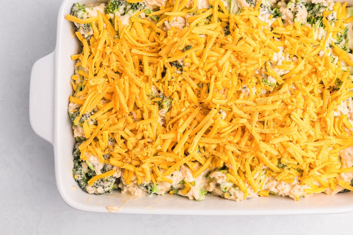 Broccoli and mixture topped with shredded cheese in a baking dish.