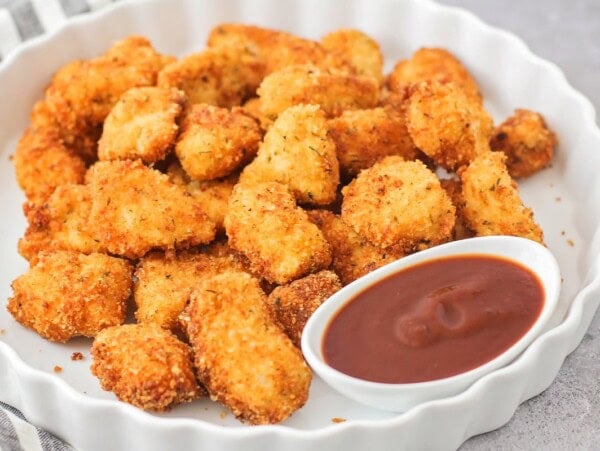 Homemade chicken nuggets on white platter with dipping sauce.