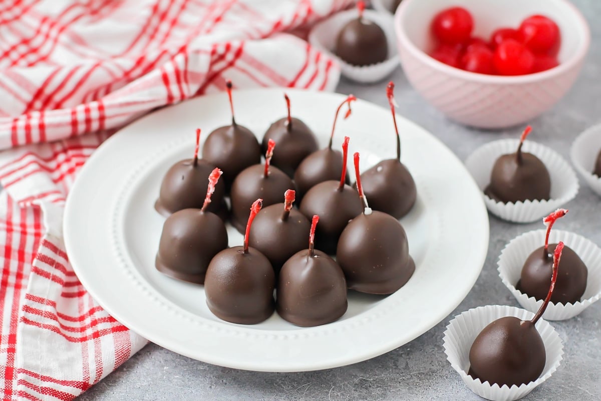 Chocolate covered cherries piled on a white plate.