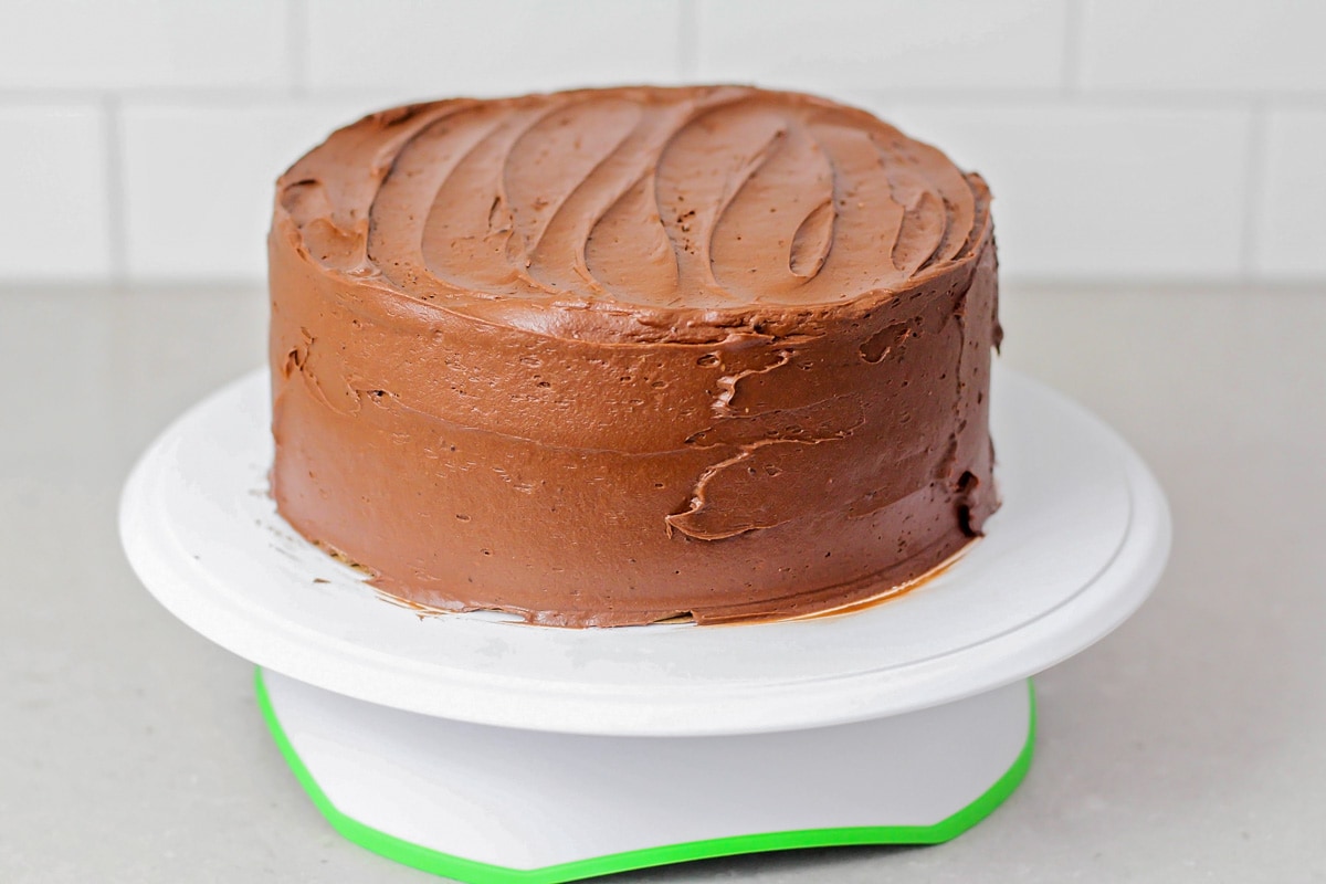 A chocolate cake covered in icing on a cake stand.
