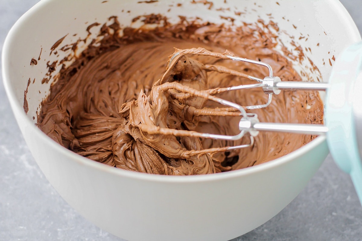 Whipping chocolate icing in a white bowl.