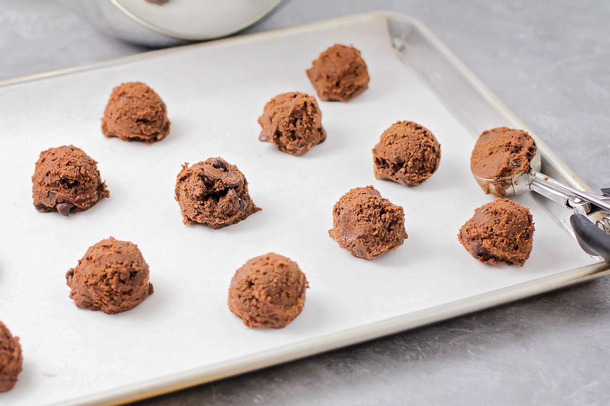 Scooping chocolate cookie dough onto a parchment line cookie sheet.