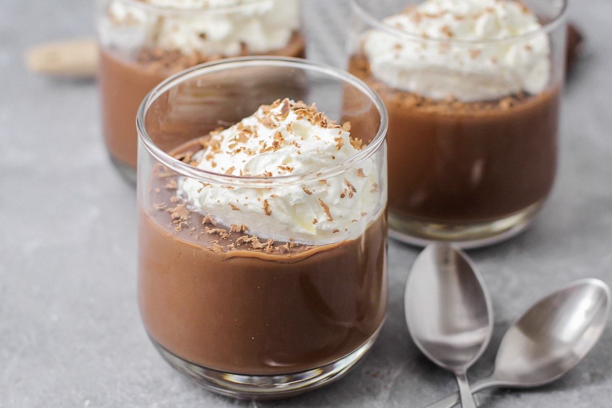 Three glass cups filled with chocolate pudding recipe topped with whipped cream.