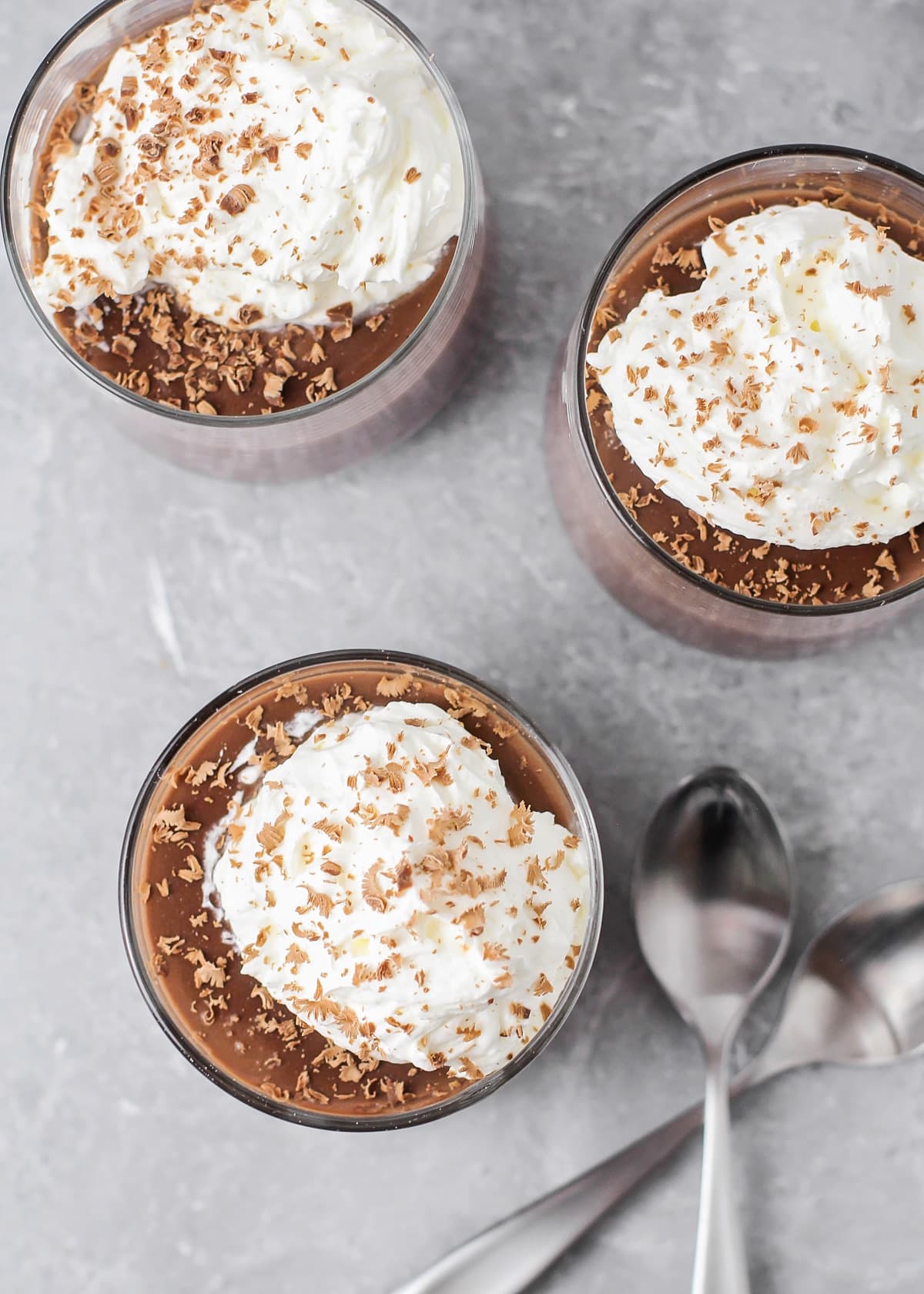 Three glass cups filled with chocolate pudding recipe topped with whipped cream.