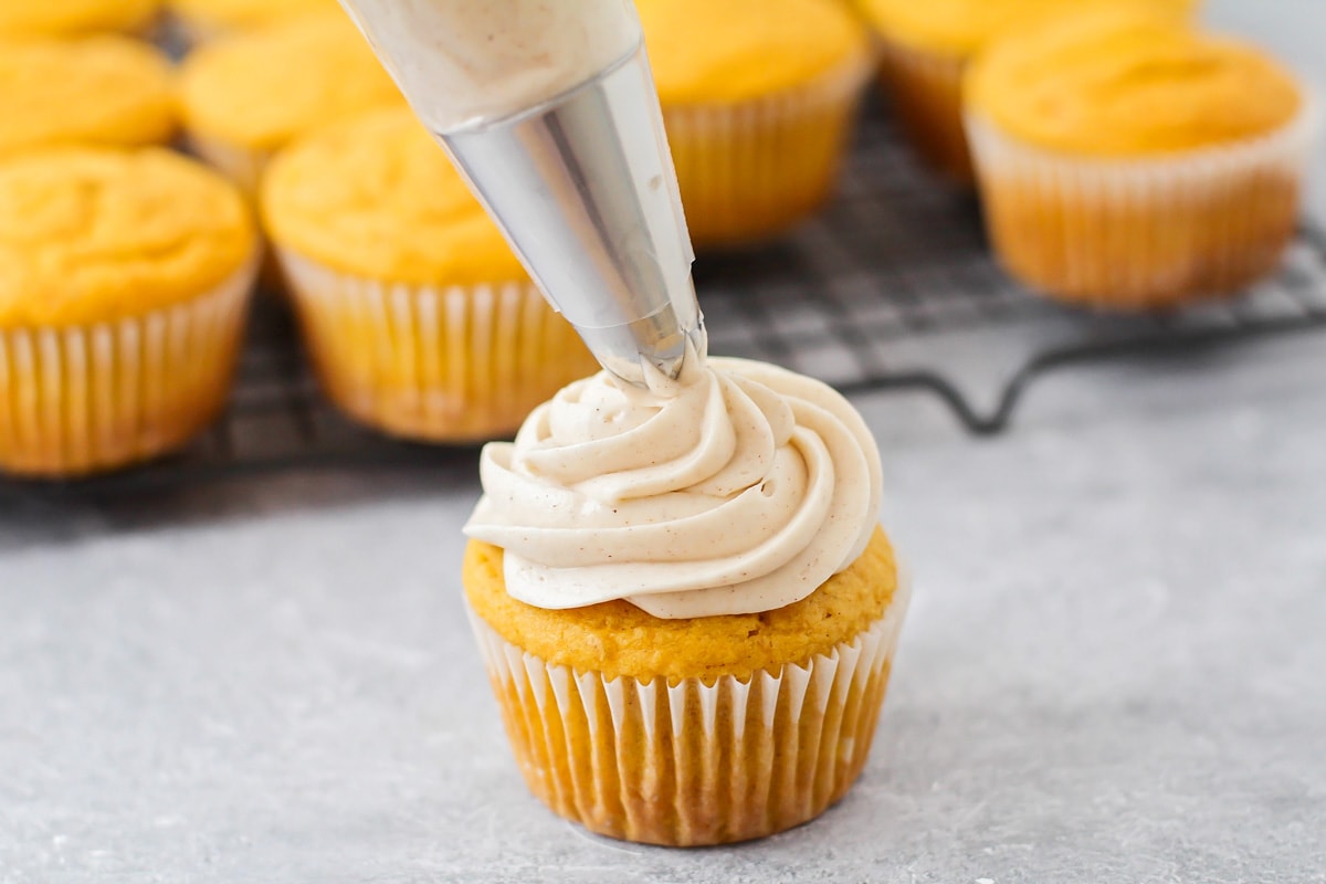 Cinnamon cream cheese frosting being piped onto pumpkin cupcake.