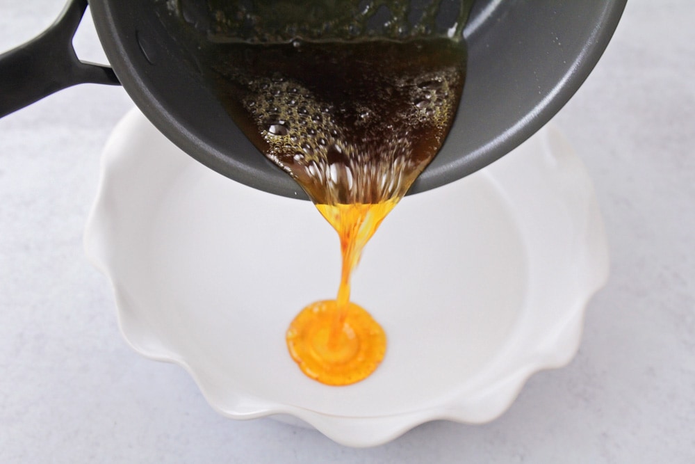 Pouring caramel into a white baking dish.