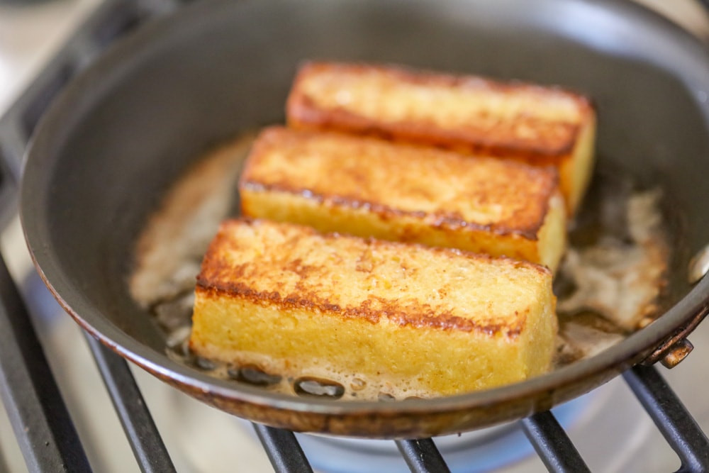 French toast sticks browning in a skillet.