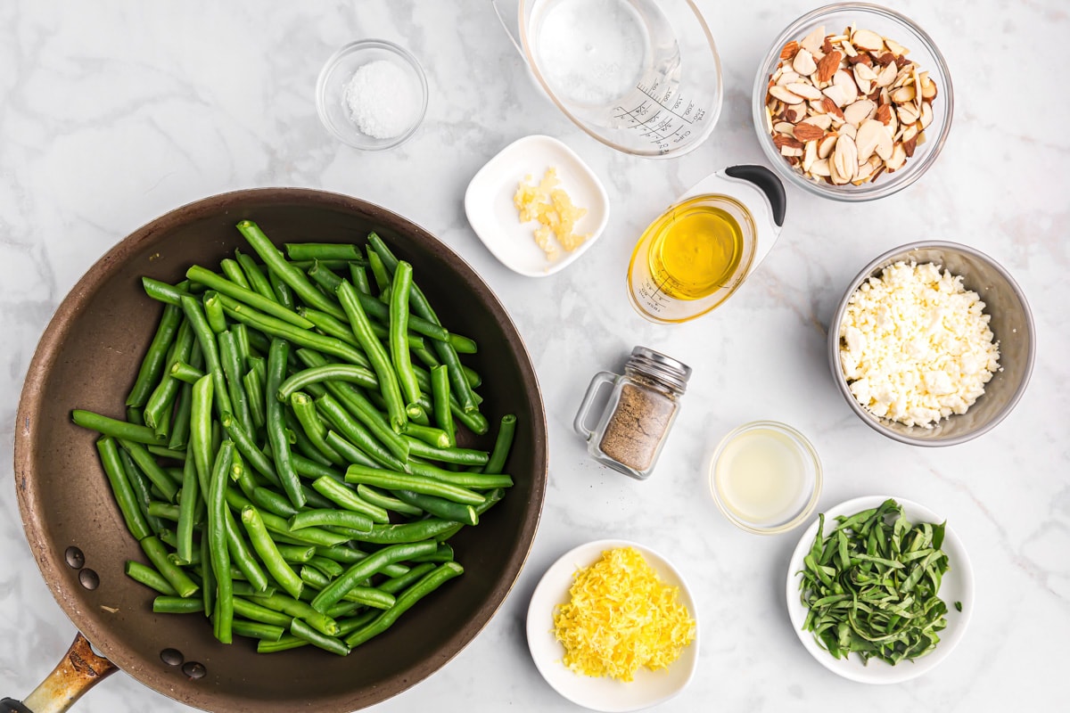 Green beans, feta, lemon zest, garlic, and almonds all measured out on a kitchen counter.