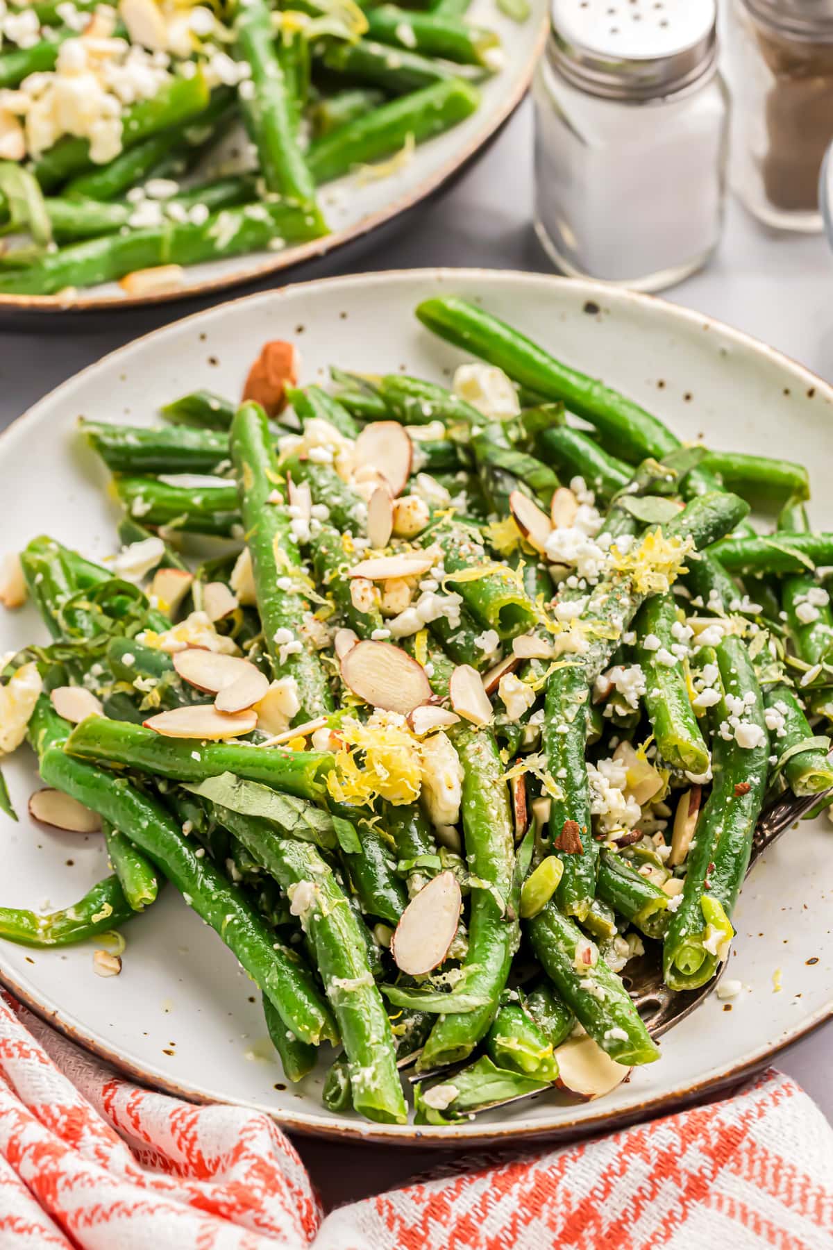 Close up of green bean salad topped with lemon zest, almond slices, and feta.