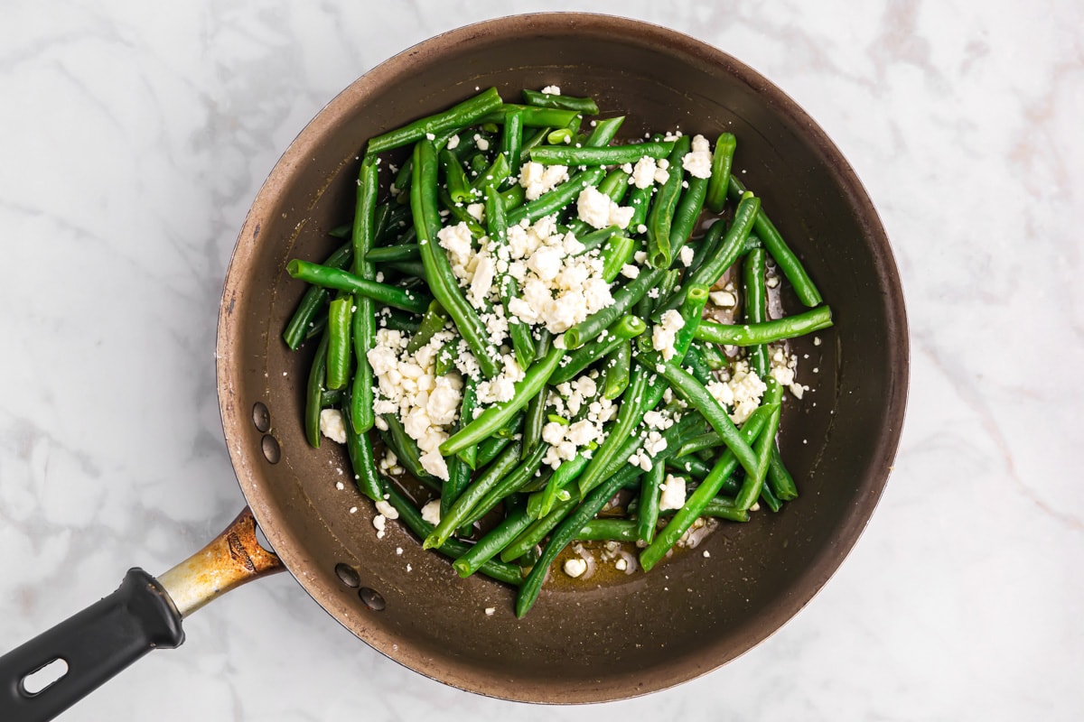 Adding feta to a skillet of cooked green beans.