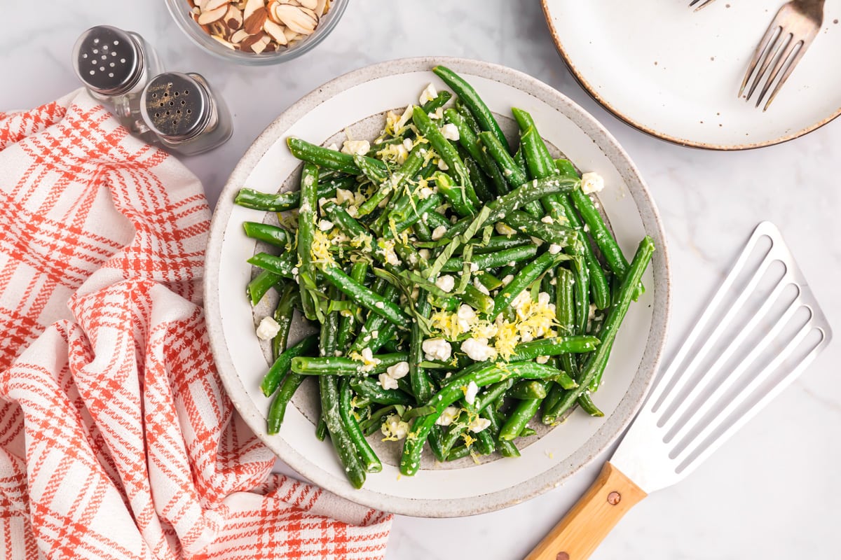 A plate of green bean salad topped with lemon zest and feta cheese.