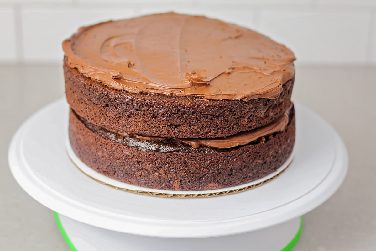 Stacking and frosting two round chocolate cakes.