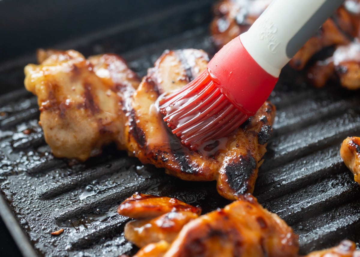 Basting grilled chicken while cooking on a grill pan.