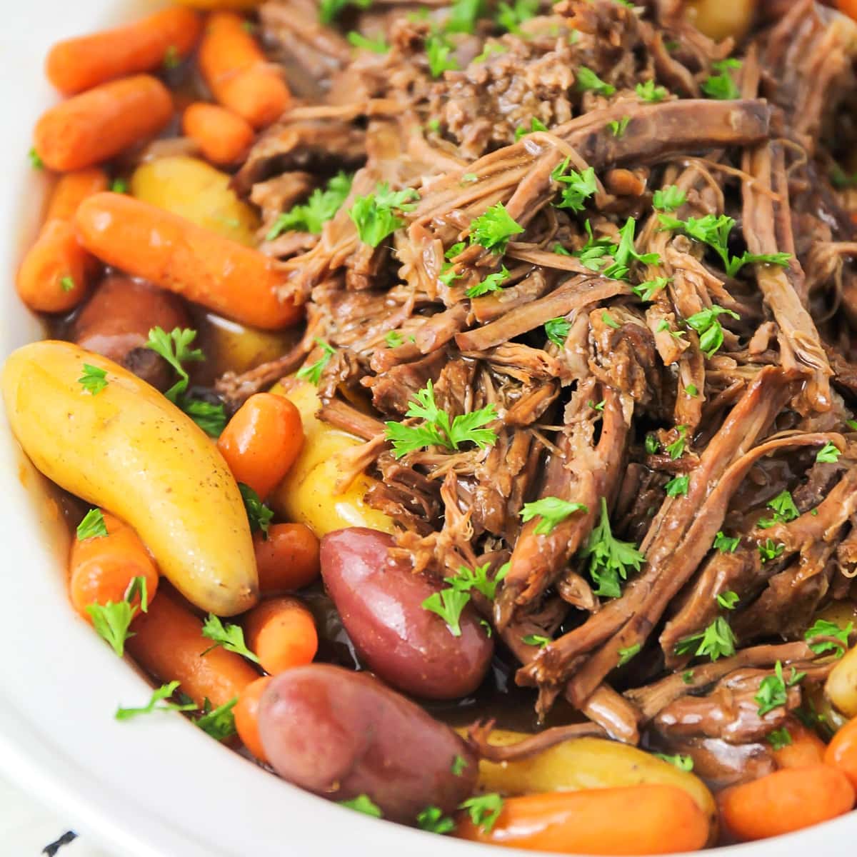 Close up of shredded meat, potatoes, and carrots in a white platter.