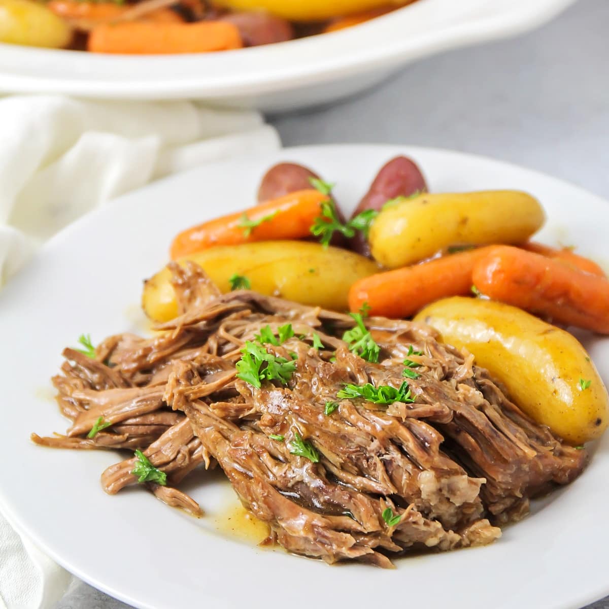 Instant pot pot roast served on a white plate with carrots and potatoes.