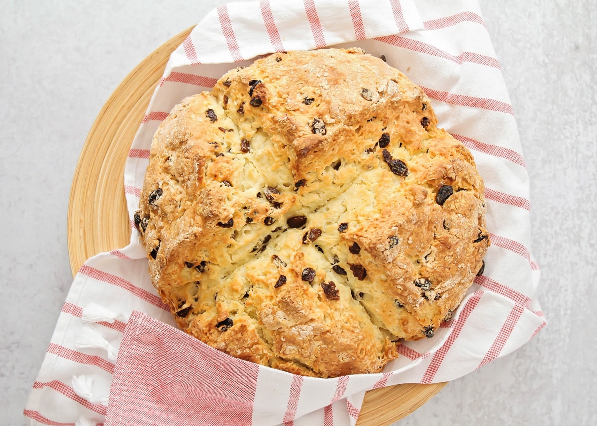 Soda bread filled with raisins and served on a red tea towel.