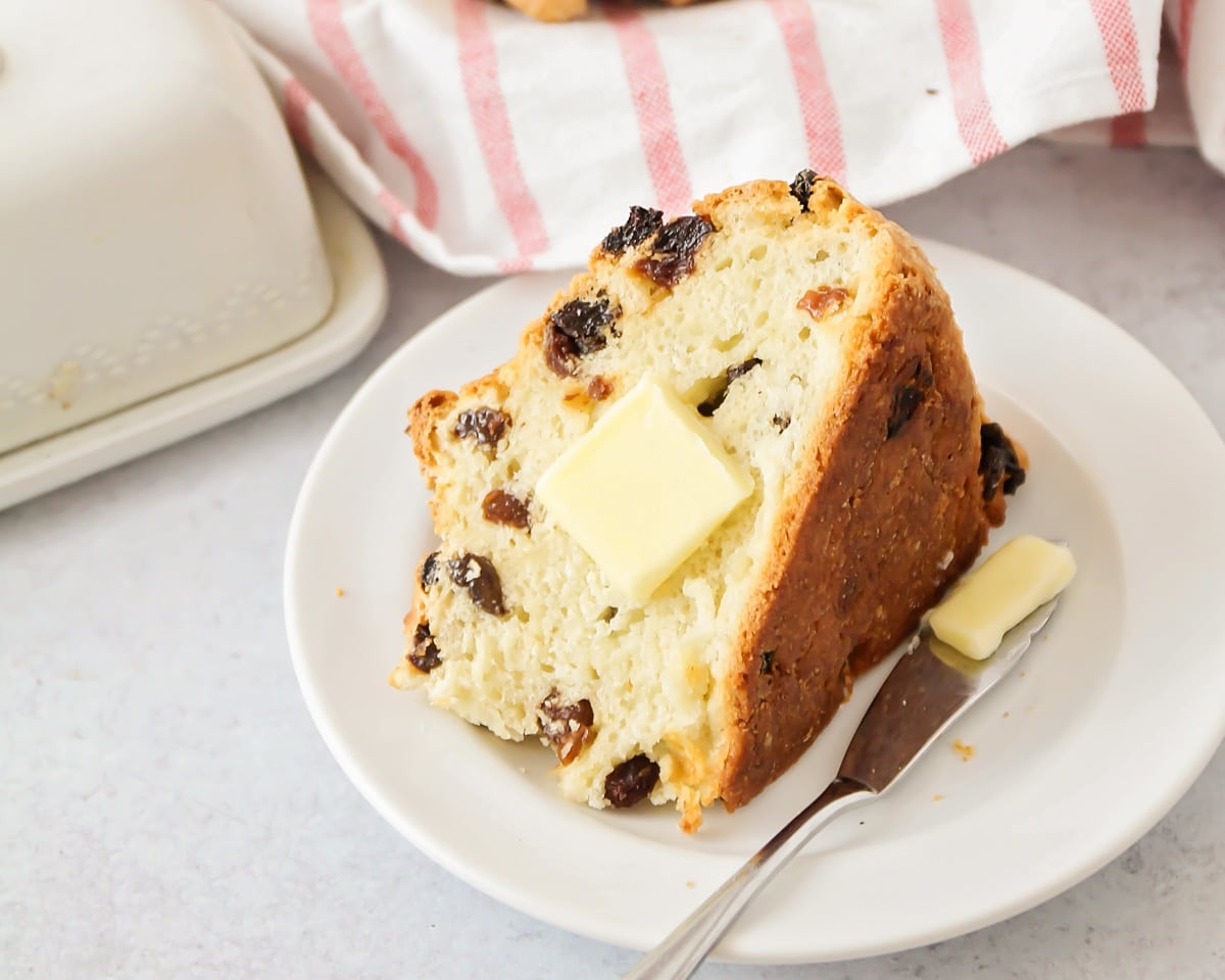 A wedge slice of raisin filled bread topped with a pat of butter.
