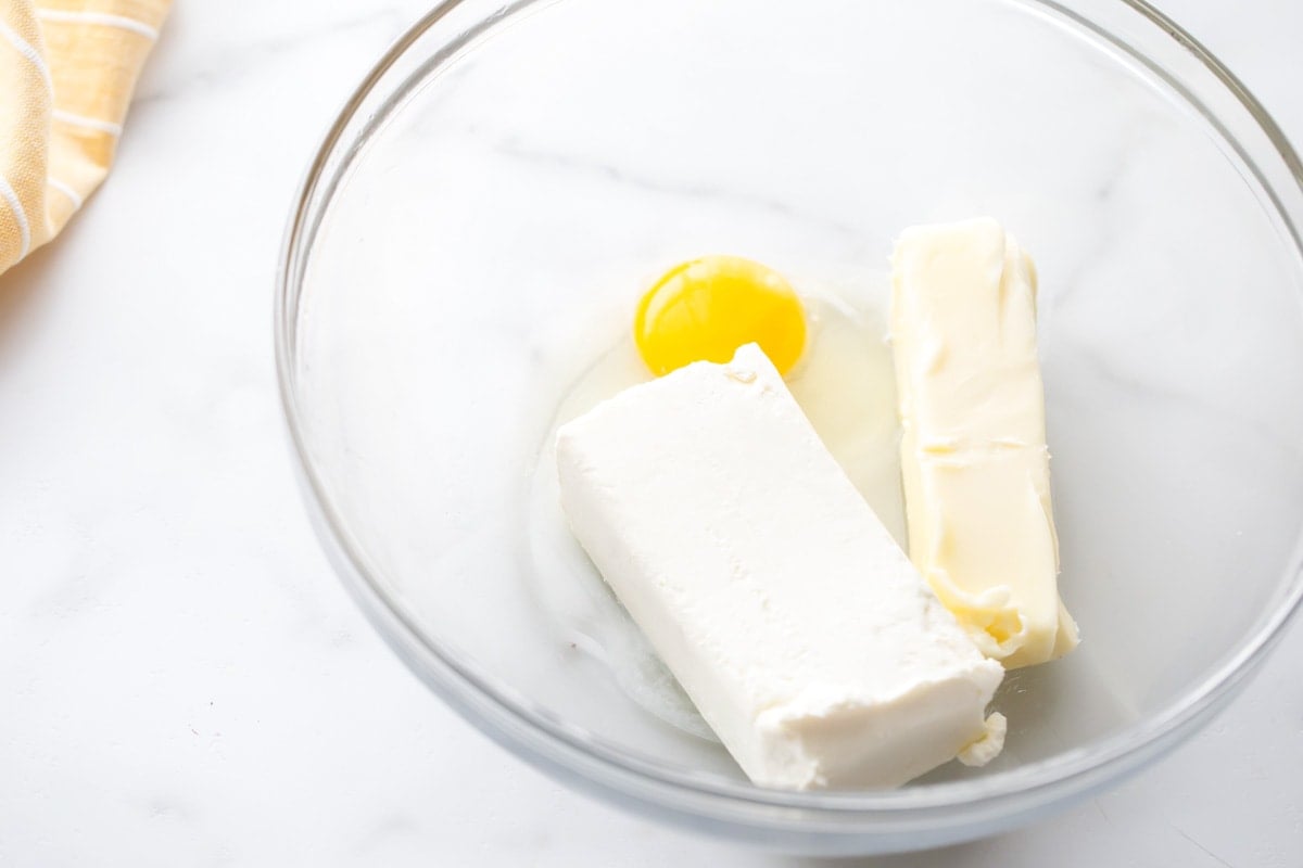 Butter, cream cheese, and an egg in a glass bowl.