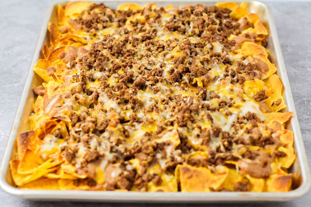 A sheet pan filled with baked tortillas, beans, ground beef, and cheese.