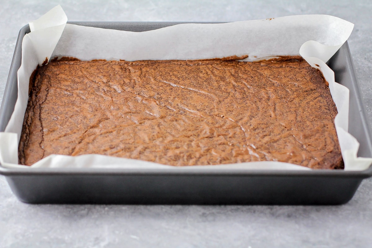 Baked brownies in a baking pan lined with parchment paper.