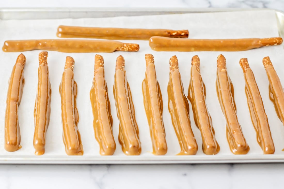 Caramel dipped pretzel rods cooling on a parchment paper lined baking sheet.