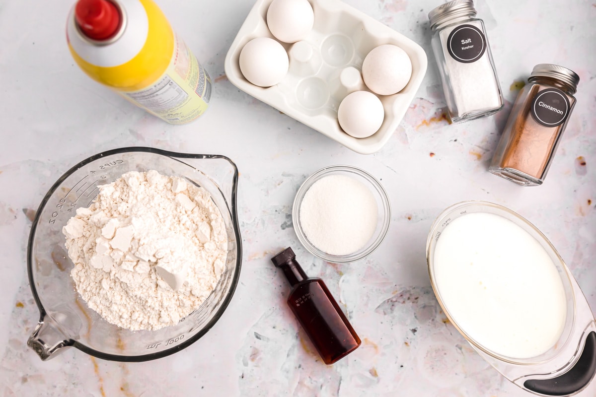 Flour, eggs, vanilla, milk, and spices measured on a kitchen counter.
