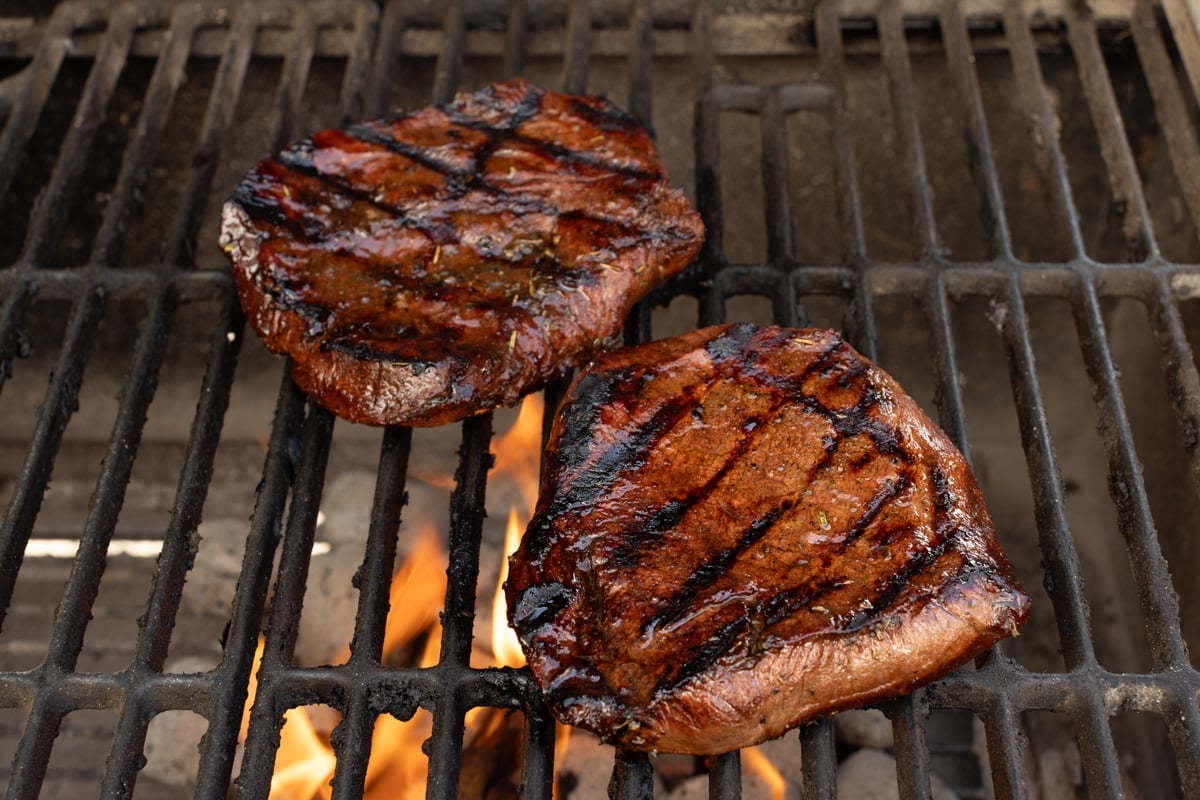 Two steaks grilling on an open flame.