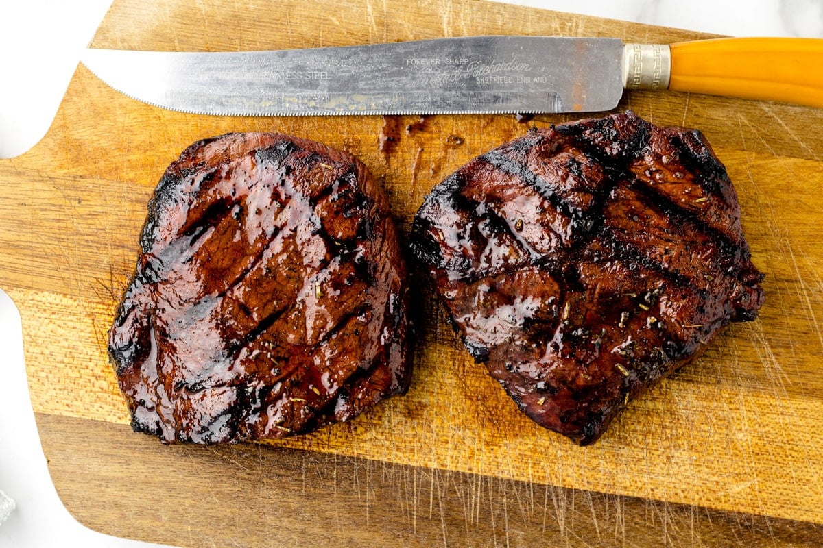 Two grilled steaks on a cutting board ready for slicing.