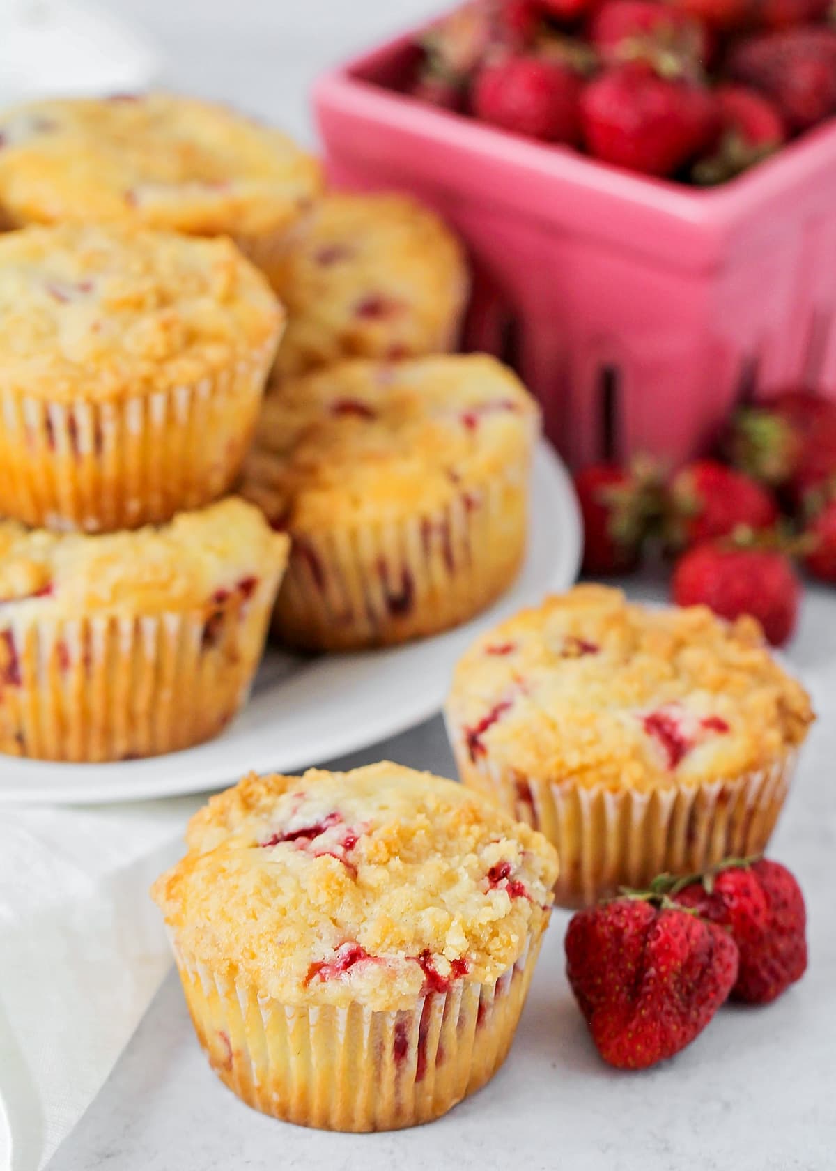 A plate of strawberry muffins with two sitting by fresh berries.