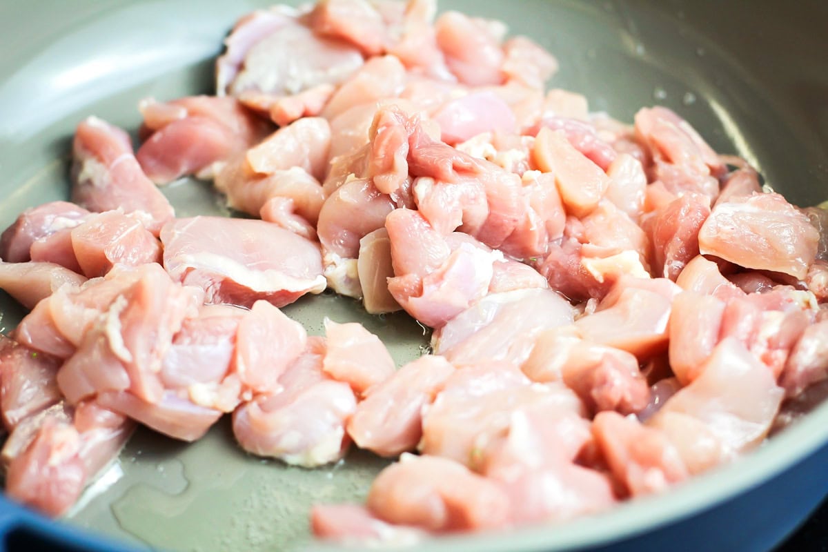 Cubed chicken thighs in skillet.