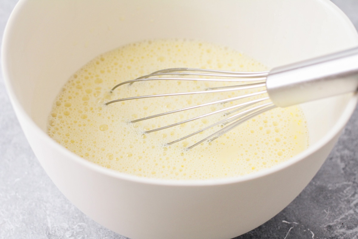 Whisking milk and eggs in a white bowl.