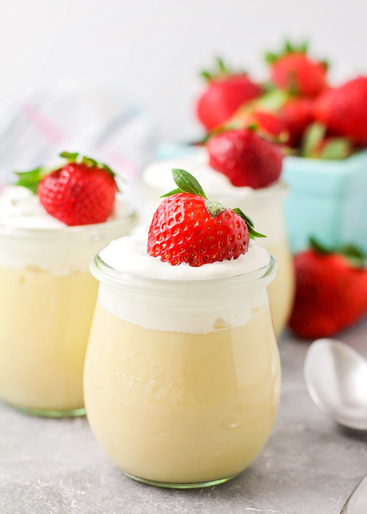 Three glasses filled with vanilla pudding recipe topped with whipped cream and strawberries.