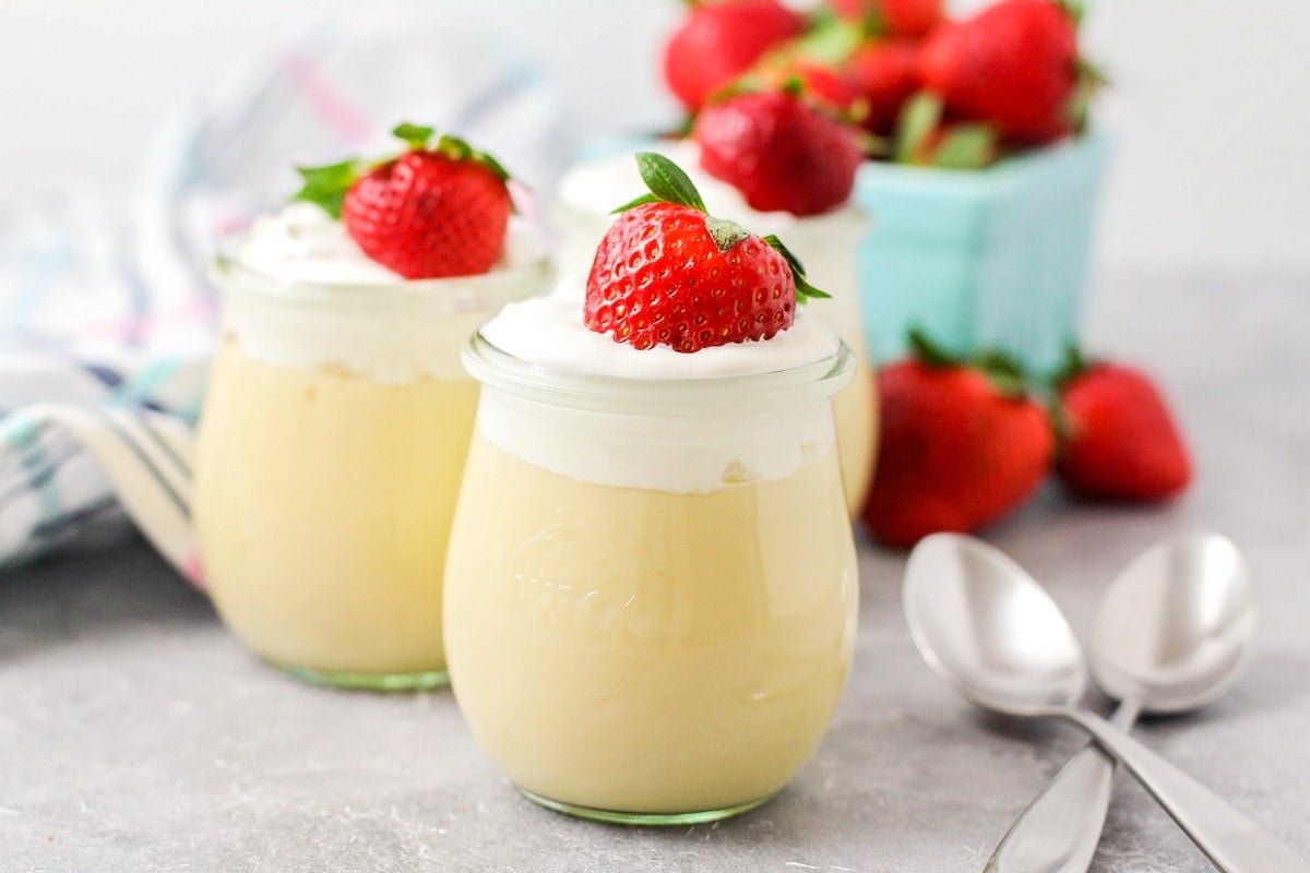 Two glasses filled with vanilla pudding recipe topped with whipped cream and strawberries.