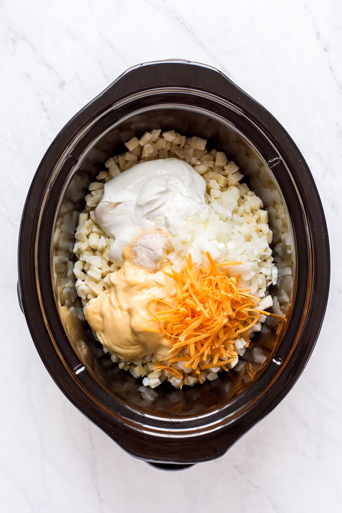 Combining hash browns, sour cream, condensed soup, and cheese in a crock pot.