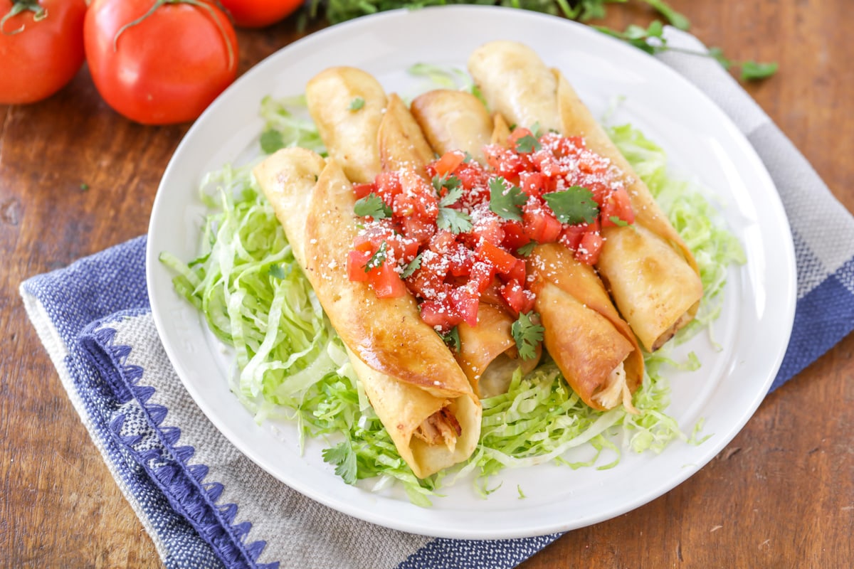 Chicken Flautas on a white serving platter with dipping sauce.