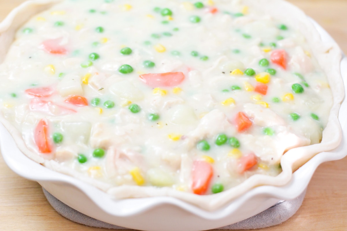 Pouring creamy chicken and veggies mixture into a blind baked pie crust.