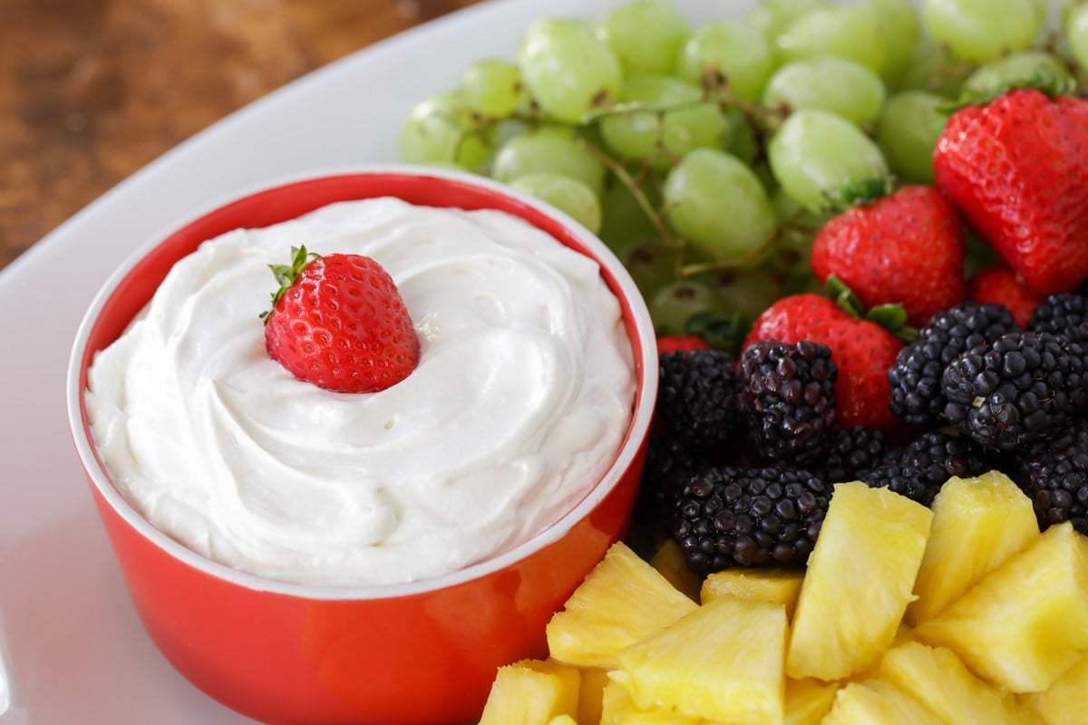 A red bowl of cream cheese fruit dip served with fresh fruit.