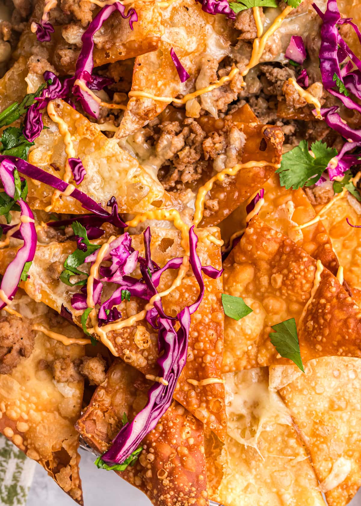 Close up of a pan of wonton nachos topped with cabbage slaw and sriracha aioli.