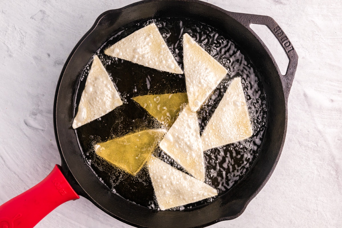 Wonton triangles frying in a cast iron skillet filled with oil.